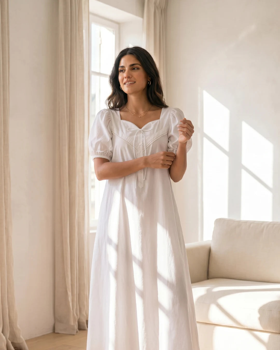 Woman in Duchess of Mayfair Sweetheart Maxi Dress Puffy Sleeve standing in a bright room with large windows.